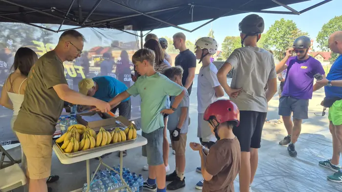 A staff member puts a wristband on a participant beside a table with water and fruit in the Ride The Future tent in Bogatynia.