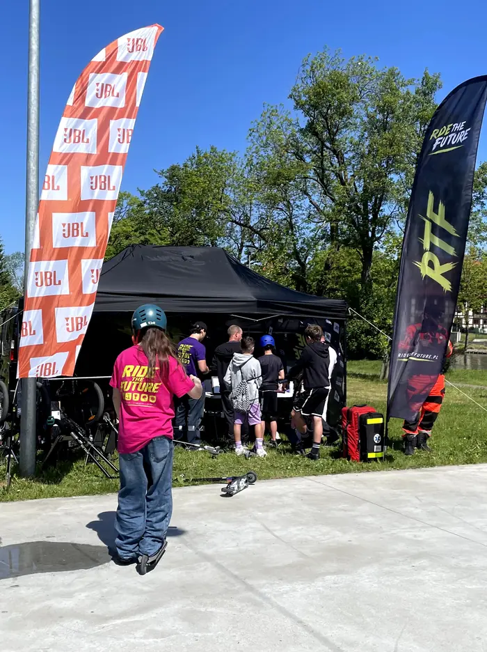 Participants and crew beside a tent framed by JBL and Ride The Future flags in Darłowo.